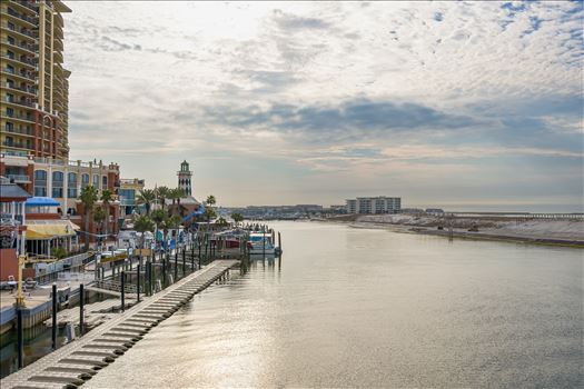 Destin Harbor's serene waters reflect the drifting clouds, with walkway, boat dock, and, condos lining the shore beneath the expansive sky.