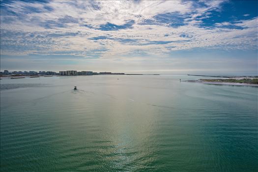 Boat departing Destin Harbor, cruising through emerald waters under a cloudy blue sky.